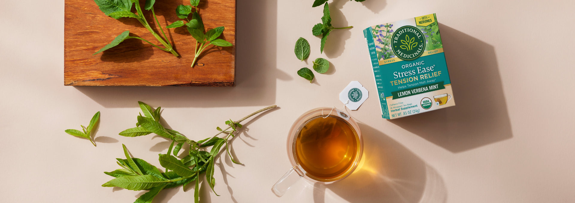 Cup of brewed tea and box of Stress Ease Tension Relief on table with herbs