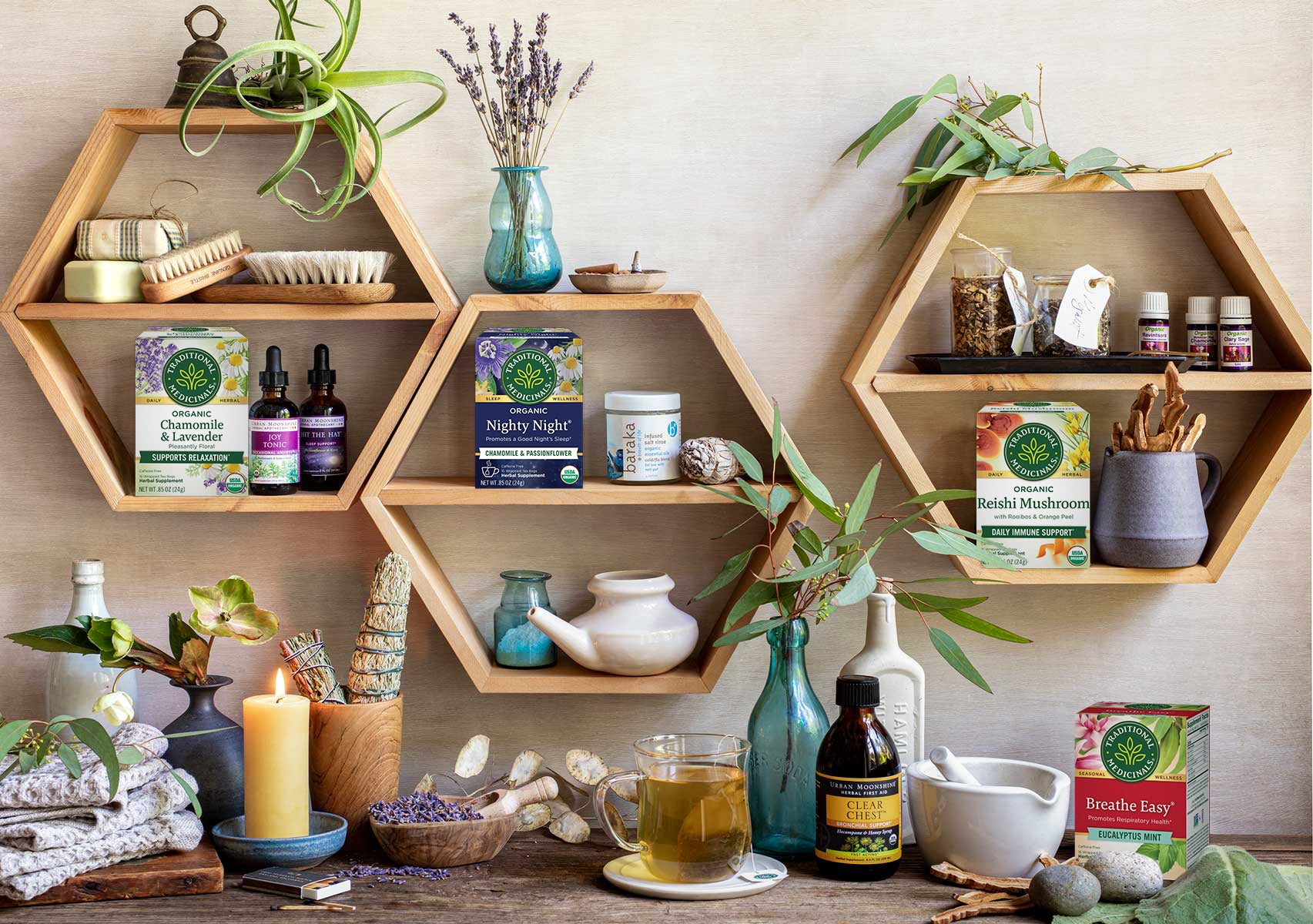 Tea boxes, tonics and plants in hexagon shelves, and candles, tea cup and apothecary items on desk